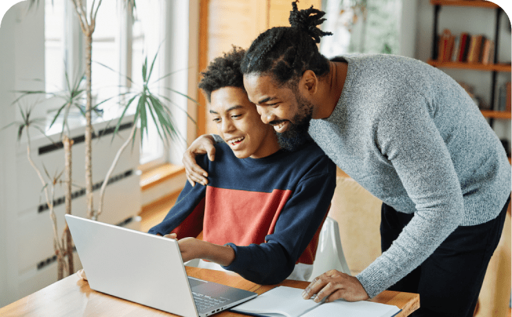 A man and a boy are intently observing a laptop screen together, sharing a moment of learning or discovery.