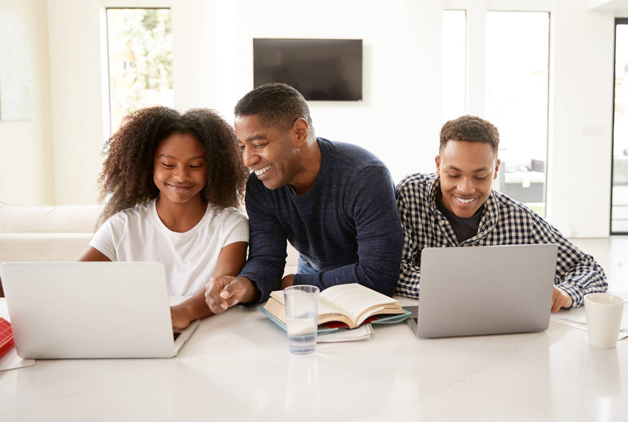 Three young individuals engaged in work at a table, each using their laptops for collaborative tasks.