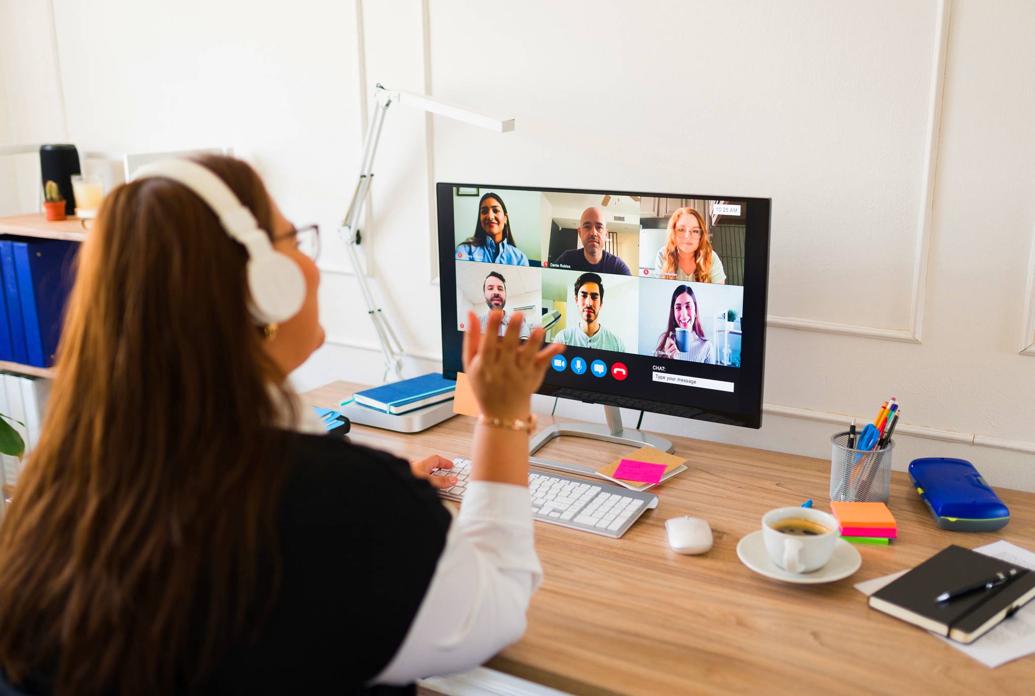 A woman at a desk, focused on a computer screen displaying multiple participants in video calls.