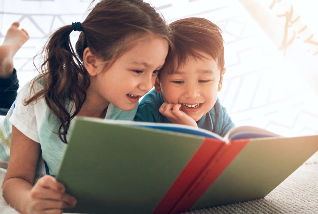 Two children sitting side by side, engrossed in reading a book together, sharing a moment of joy and learning.