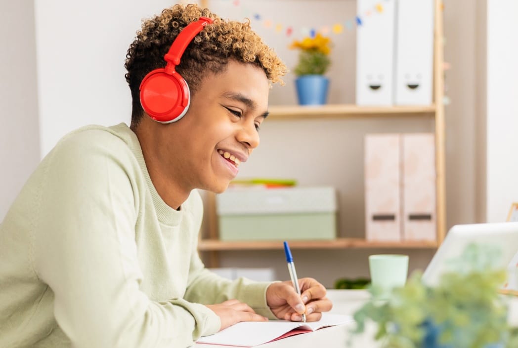 A young man wearing headphones is focused on working on his laptop at a desk.