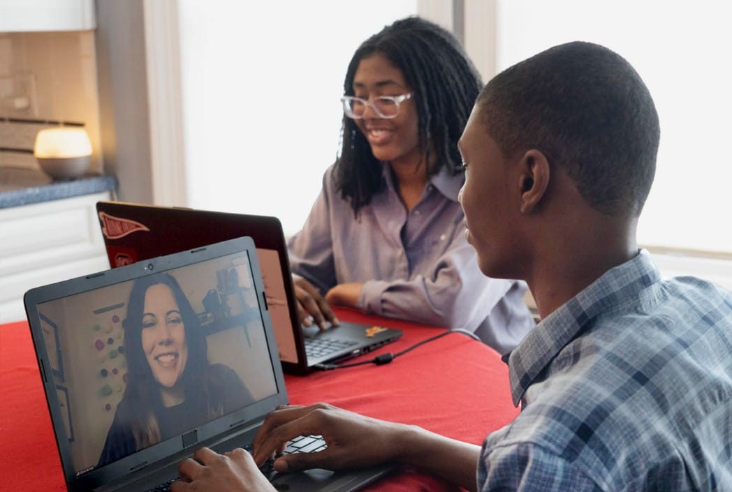 Mother and son seated at a table, each using a laptop, engaged in a collaborative work session.