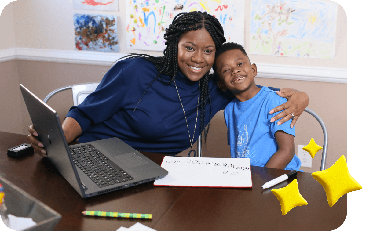 Smiling woman and child sit at a table with a laptop, drawings in the background. The child holds a whiteboard with scribbles. Their expressions are joyful.