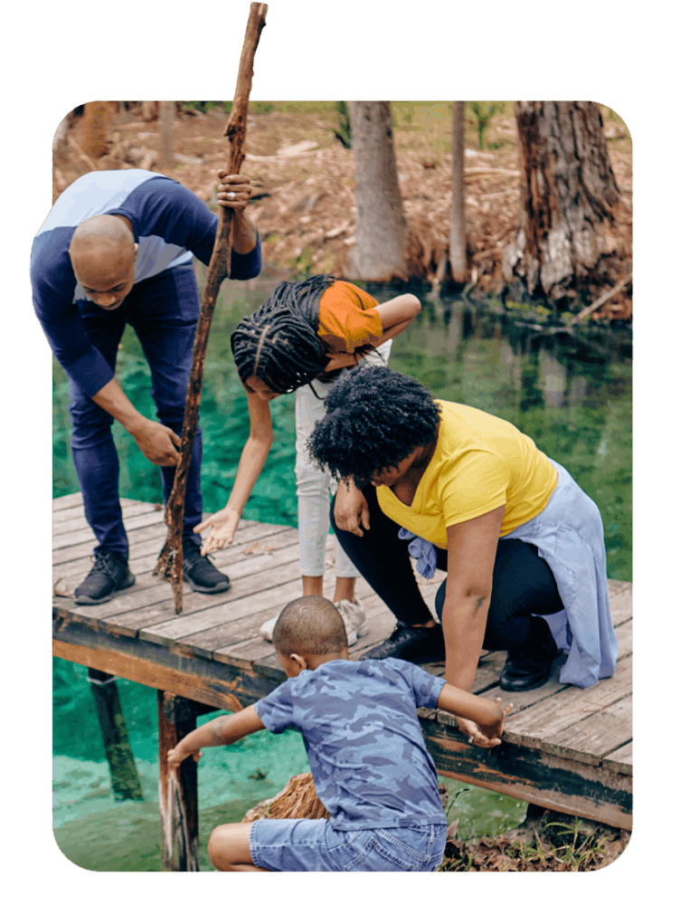 A family of four engages with nature on a wooden dock above clear turquoise water. They lean forward curiously, fostering a sense of exploration and bonding.