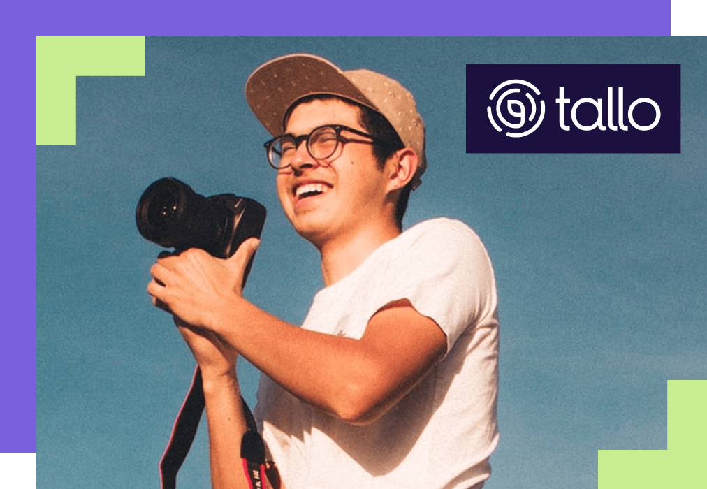 A person wearing glasses and a cap holds a camera, smiling at the sky, suggesting creativity and joy. The Tallo logo is in the top right corner.